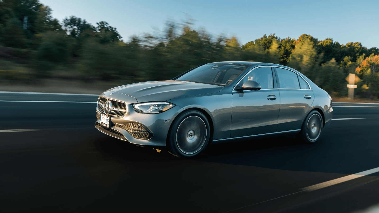 Mercedes sedan in motion on a highway, autumn trees in background